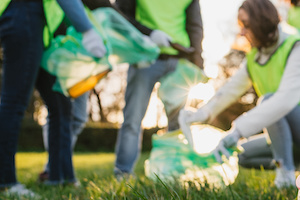 Group of friends during a volunteer garbage collection event in a park at sunset - Millennial having fun together - Happy people cleaning area with bags - Ecology concept